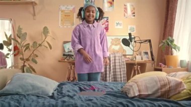 Orta boy Afro-Amerikan genli kız kablosuz kulaklık takıyor, canlı çocukların yatak odasında dans ederken eğleniyor.