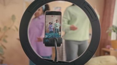 Çift cinsiyetli genç anne ve 10 yaşındaki kızı tripoda ve halka ışığına akıllı telefon kullanarak çocukların yatak odasında dans ederken çekilmiş son moda videolarını kaydediyorlar.