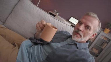 Kafkasyalı bir iş adamının kanepede oturup rahatça kahve içerken videosunu kaydettiği el bilgisayarı görüntüsü.