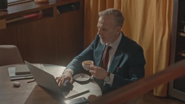 上图拍摄的是一位成功的白种人商人在餐馆工作时穿着雅致的西装 一边喝咖啡 一边在笔记本电脑上打字 — 图库视频影像