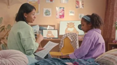 Elinde matematik kâğıdı olan orta sınıf bir kadının 10 yaşındaki kızına çalışmasında yardım ederken, sıcak çocuk odasında yatağında otururken.
