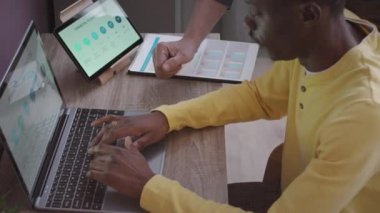 Ofiste iş sunumu üzerinde çalışırken dizüstü bilgisayar ve tablet bilgisayar kullanan iki çok ırklı erkek arkadaşın görüntüsü.