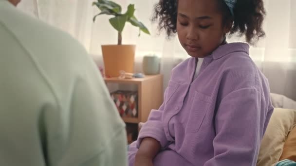 近くに座っている有用な母親と自宅でベッドで学校の宿題をしているスマートなアフリカ系アメリカ人の少女のティルトショット — ストック動画