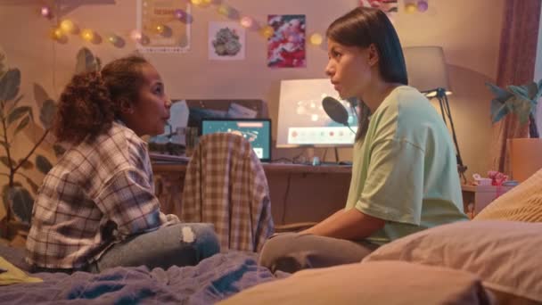 若いBiracialの女性と彼女のクールなプリーツの娘が夜遅く居心地の良いキッズベッドルームでベッドに座って会話 — ストック動画