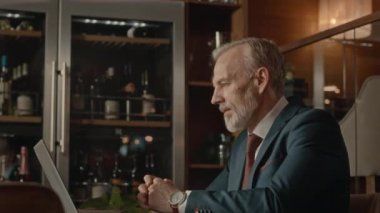 Orta yaşlı, zarif takım elbiseli beyaz iş adamının belden yukarısında dizüstü bilgisayarda konferans videosu. Restorandaki ahşap masada oturuyor.