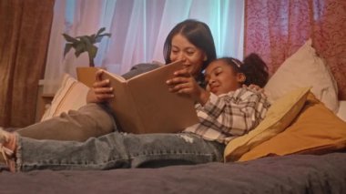 Afrika kökenli Amerikalı anne ve küçük kızı çocuk odasında rahat bir yatakta kitap okuyorlar.