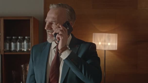 中年白胡子商人穿着雅致的蓝色西服 站在豪华办公室用智能手机交谈的中景照片 — 图库视频影像