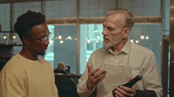 아프리카계 미국인 고객에게 그것을 제시하는 와인의 레스토랑에서 일하는 성숙한 소믈리에의 — 비디오