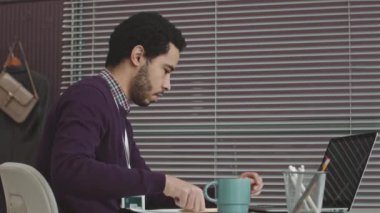 Orta Doğulu genç bir erkek programcının ofis masasında çalışırken dizüstü bilgisayar kullanmasının belden yukarı görüntüsü.