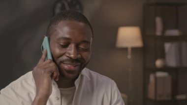 Modern ev ofisinden çalışırken akıllı telefondan konuşan genç siyahi adam.