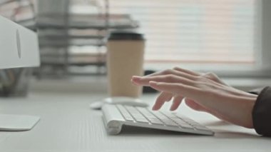 Ofiste çalışırken beyaz kablosuz klavyeye yazı yazan kadın programcının tanınmayan ellerine yakın çekim