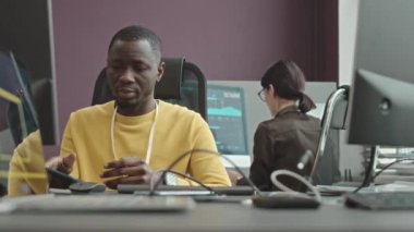 Programlama ofisinde kadın meslektaşımla bilgisayar üzerinde çalışırken genç konsantre siyah erkek yazılım mühendisinin kablosuz klavyeye yazması