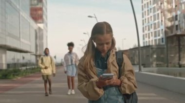 Yaz mevsiminde çeşitli sınıf arkadaşlarıyla yürürken akıllı telefon kullanan Kafkasyalı güzel bir kızın orta boy fotoğrafını çekiyorum.