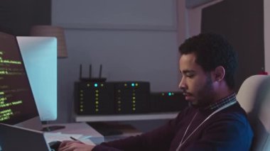 Orta Doğulu erkek yazılım mühendisinin karanlık sunucu odasında masaüstü bilgisayarı ve dizüstü bilgisayarı üzerinde çalıştığı belden yukarısı