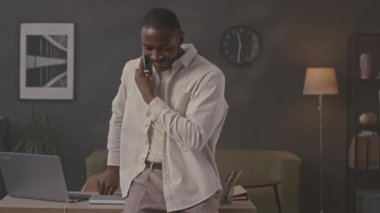 Genç Afrikalı Amerikalı iş adamının minimalist ofiste telefon konuşması yaparken orta boy bir fotoğraf.