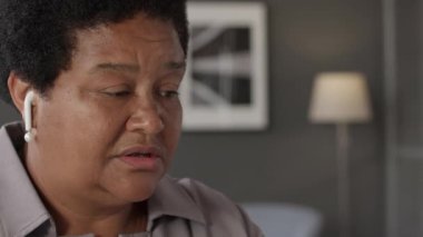 Orta yaşlı başarılı Afro-Amerikan kadının bilgisayar ve kablosuz kulaklıkla iş ortağıyla konuştuğu, gündüz masasında oturduğu orta boy yakın plan.