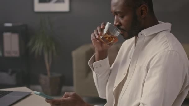 Pas Górę Czarnego Przedsiębiorcy Pijącego Whisky Przeglądającego Smartfonie Podczas Pracy — Wideo stockowe