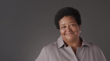 Koyu gri arka planda kameraya gülümseyen yetişkin Afro-Amerikan kadın portresi.
