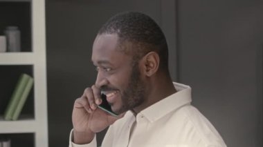 Yakışıklı zenci adam cep telefonuyla konuşuyor ve minimalist ofiste çalışırken pencere perdelerinden bakıyor.