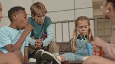 Orta boy ergen erkek ve kız çocuklarının okul yemeği yerken sohbet edişleri açık havada merdivenlerde oturmaları.