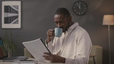 Ofis masasında kameraya poz veren başarılı Afrikalı Amerikalı iş adamının orta boy portresi.