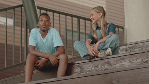Kaukaski Nastolatek Dziewczyna Siedzi Drewnianych Schodach Zewnątrz Rozmawia Afroamerykanin Mężczyzna — Wideo stockowe