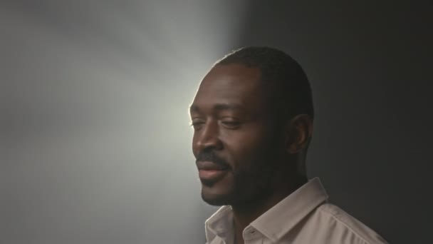 카메라와 미소에 손바닥을 보여주는 배경에서 위에서 빛나는 스포트라이트 남자의 스튜디오 — 비디오