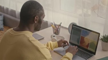 Genç yetişkin siyahi adamın ev ofisinden bağımsız olarak çalışırken dizüstü bilgisayar kullanışının arka planı