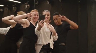Siyah beyaz giyinmiş, çok ırklı neşeli dans üçlüsü antrenman sırasında akıllı telefon kamerasında komik selfie portreleri çekerek balo salonunda eğleniyor.