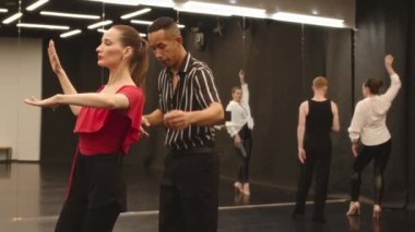 Geniş dans sınıfında Melez erkek öğretmenden ders alırken kırmızı bluz giyen ve dudaklarını Latince dans hareketlerine alıştıran beyaz bir kadın.