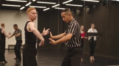 Beyaz erkek dans hocasının, grup dans derslerine katılan çift ırklı bir adama Latin dansı hareketleri göstermesi.
