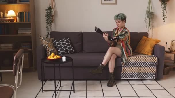 居心地の良いリビングルームでソファーに座っている間 彼女の腕の義足を寄付する白人少女 — ストック動画