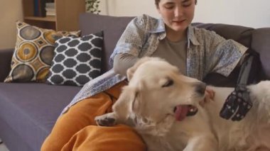 Kafkasyalı, protez kollu genç bir kızın evdeki kanepede sevimli köpeğiyle oynadığı resimden.