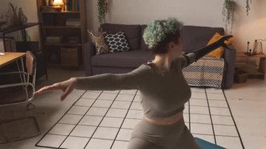 20 'li yaşlarının başında protez kollu beyaz bir kızın evde tek başına yoga yaptığı orta boy bir fotoğraf.