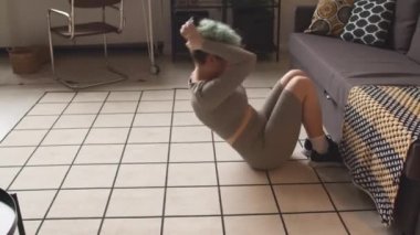 Yapay kollu beyaz bir kız mekik çekerken kanepe kullanıyor, evde karın kasları çalışıyor.