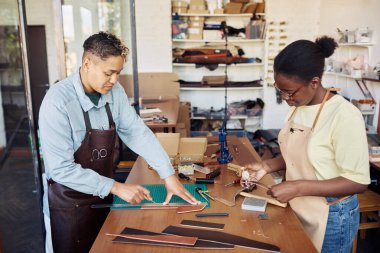 Leatherwork atölyesinde çalışan ve el yapımı çantalar yapan iki genç kadının yüksek açılı portresi.