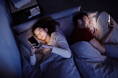 Yatmadan önce akıllı telefon kullanan genç çiftin yüksek açılı görüntüsü.