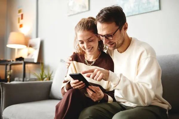 Young couple watching funny video on smartphone during their leisure time on on sofa at home