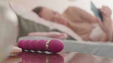 Kafkasyalı genç bir kadın komodininden pembe vibratör alıyor ve sabah tek başına yatakta dinleniyor.