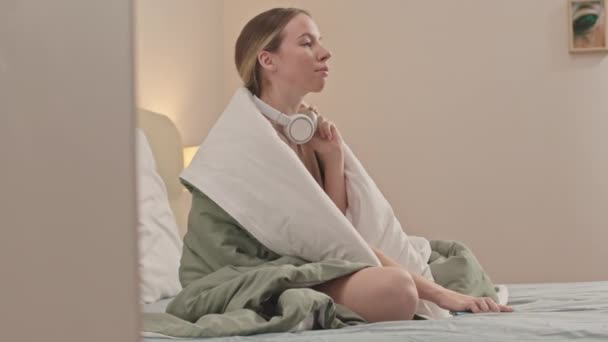 Кавказька Дівчина Слухає Танцює Музику Бездротових Білих Навушниках Сидячи Ліжку — стокове відео