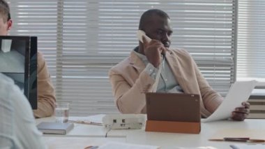 Modern ofisteki çeşitli iş arkadaşlarıyla çalışırken Afrika kökenli Amerikalı erkek güvenlik şefi telefon görüşmesi yapıyor.