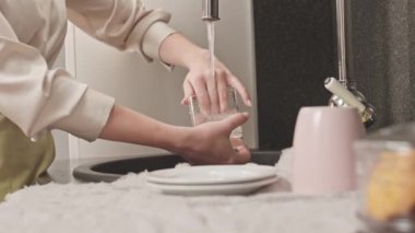 Gündüz vakti mutfak lavabosunda bulaşık yıkayan tanınmayan bir kadının görüntüsü.