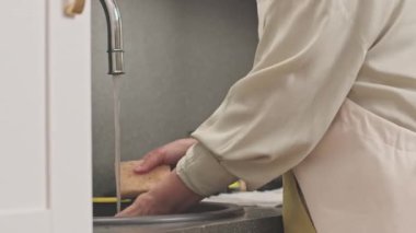 Evdeki mutfak lavabosunda bulaşık yıkarken sünger kullanan tanınmayan bir kadının görüntüsü.