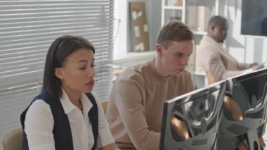 Çift ırklı kadın güvenlik müdürü ve çok ırklı erkek meslektaşları modern ofiste masaüstü bilgisayarlarının başında oturup video güvenlik kameralarını izliyorlar.