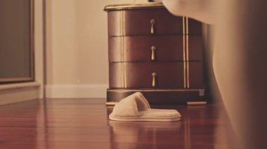 Sabahları yataktan çıkarken kısa beyaz çoraplı, yumuşak terlik giyen, tanınmayan bir kadının alt kısmı.