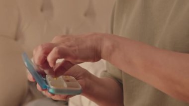 Yaşlı Asyalı kadın gece uyumadan önce vitamin ve ilaç alıp karanlık odada oturuyor.