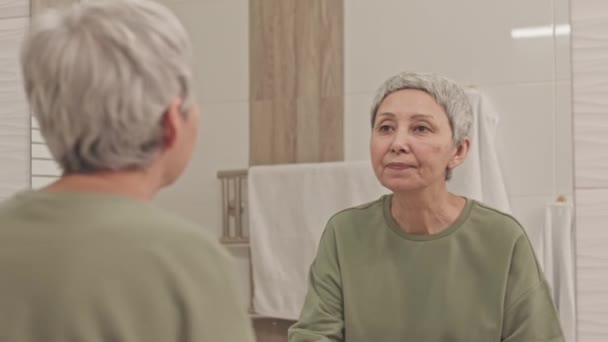 Snygg Mogen Asiatisk Kvinna Undersöker Hennes Reflektion Spegel När Står — Stockvideo