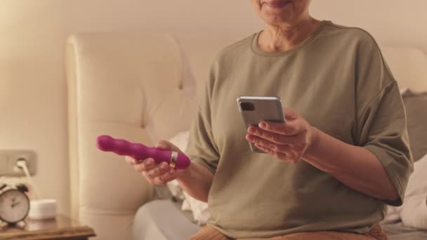 Przycięte Zdjęcie Starszej Kobiety Siedzącej Samotnie Domu Smartfonie Fioletowym Wibratorem — Wideo stockowe