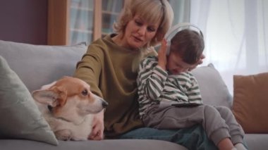 Kafkasyalı mutlu, sarı saçlı kadın evde kalıyor. Down sendromlu küçük oğluyla. Şirin Corgi köpekleri, parlak oturma odasındaki kanepede birlikte dinleniyor.