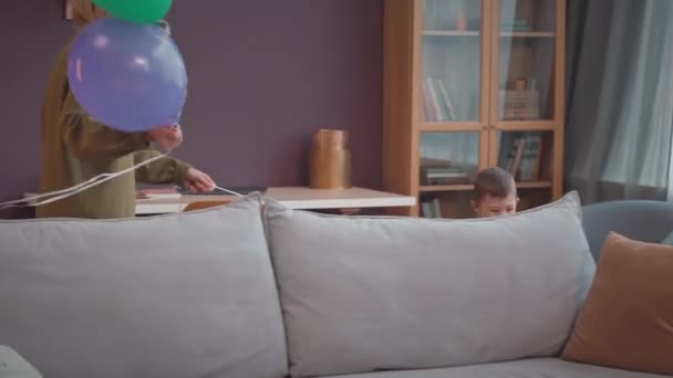 快乐的小男孩与他快乐的妈妈一起在明亮的客厅里与五颜六色的派对气球玩耍 — 图库视频影像
